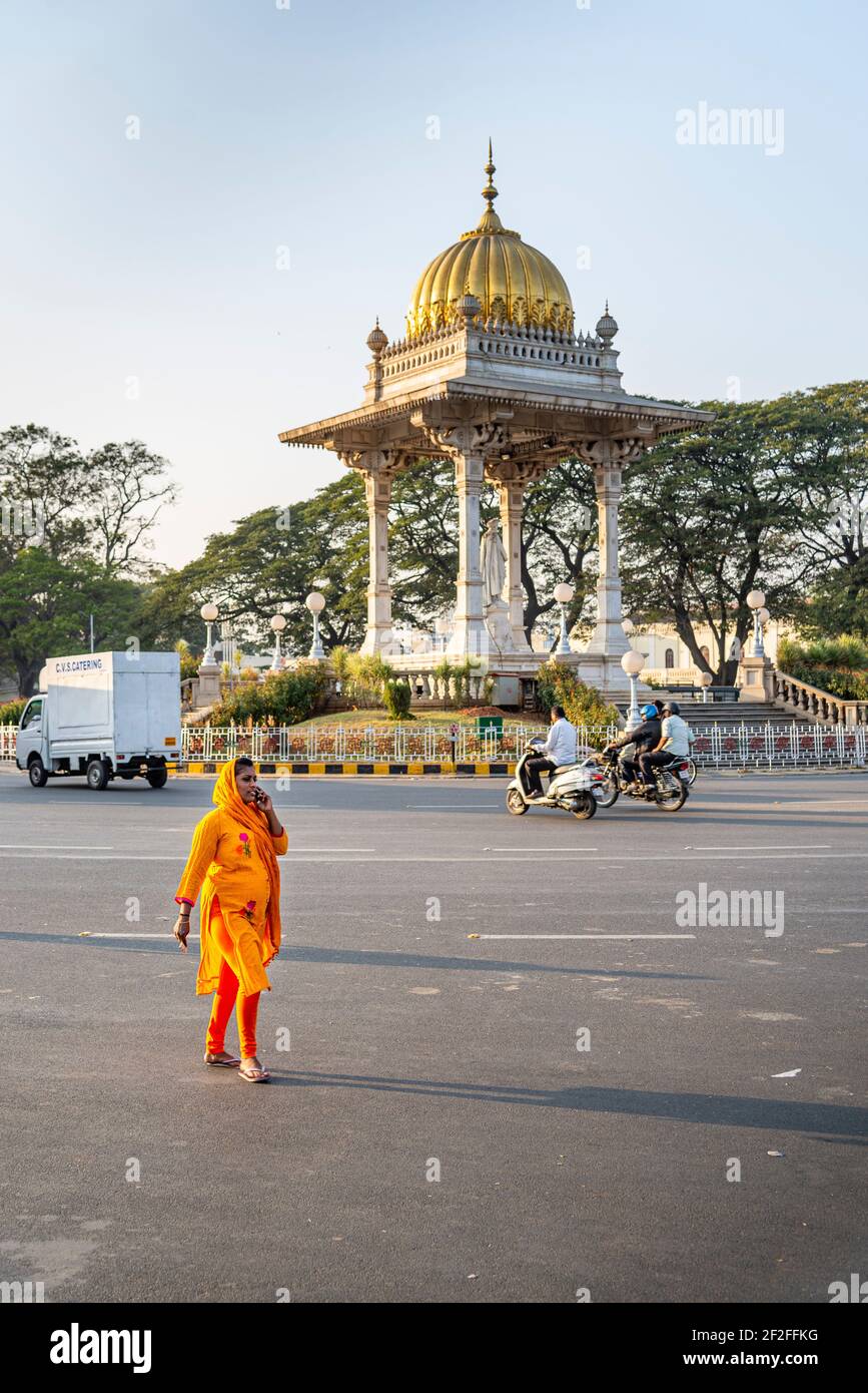 Femme dans le kurta orange marche à l'intersection en face du palais à Mysore, Inde Banque D'Images
