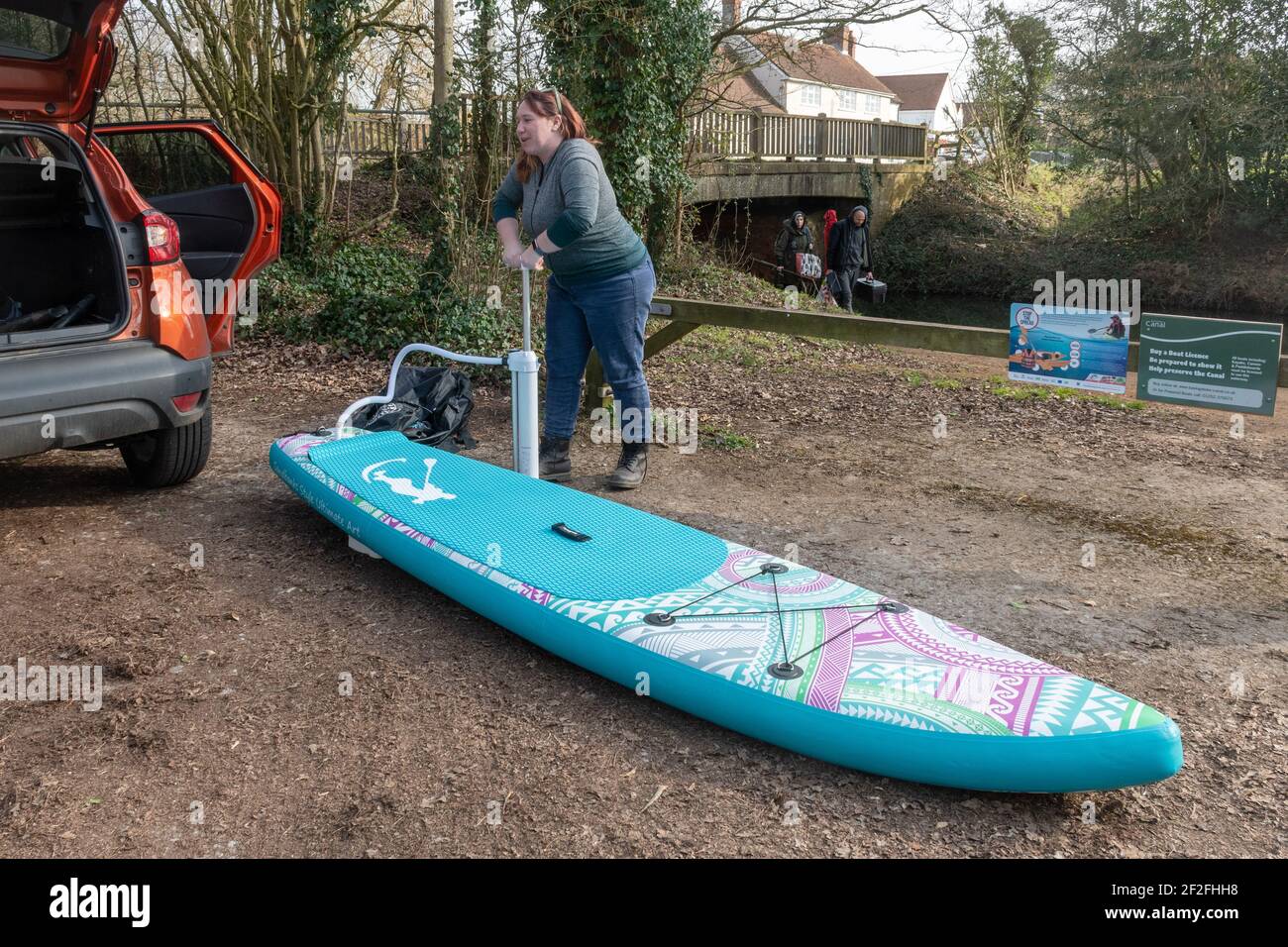 Femme gonflant un panneau de paddle board (SUP) avec une pompe manuelle à côté d'un canal, Royaume-Uni Banque D'Images