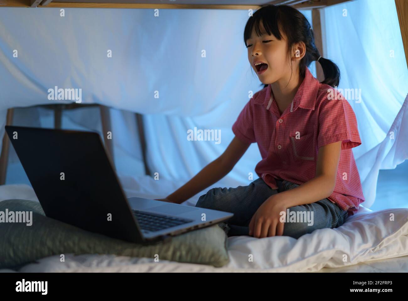 Une fille asiatique à faire un camp pour jouer de façon créative en regardant un film sur ordinateur portable dans l'obscurité du camp dans le salon à la maison. Banque D'Images