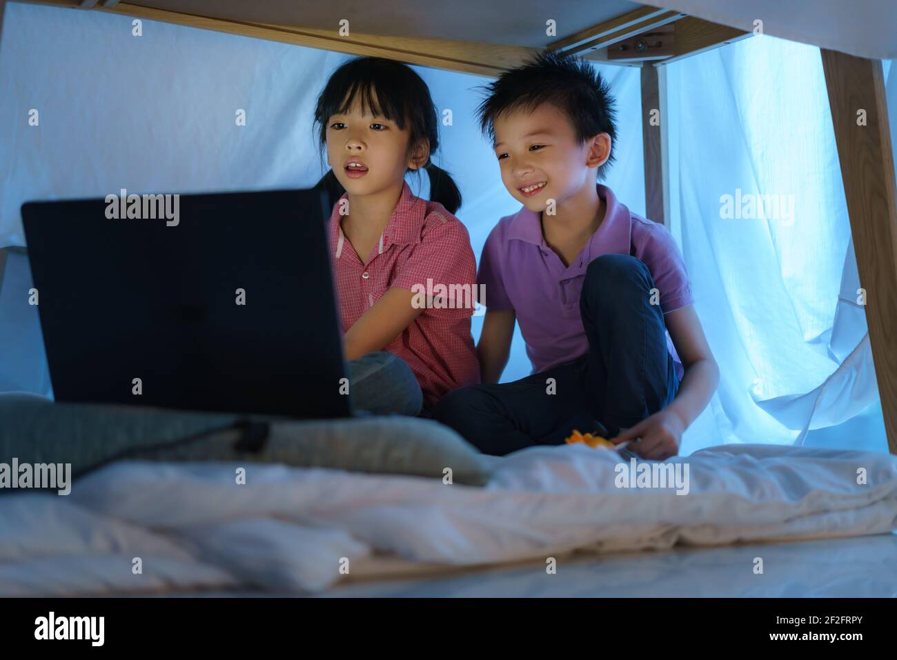 Enfant asiatique et sa sœur à faire un camp pour jouer avec imagination en regardant un film sur ordinateur portable dans l'obscurité du camp dans le salon à la maison. Banque D'Images