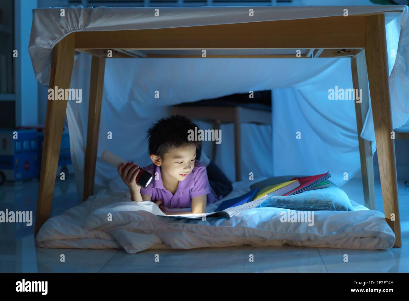 Enfant d'âge préscolaire asiatique faire un camp pour jouer imaginatif et lire livre par lampe de poche dans le salon à la maison. Banque D'Images