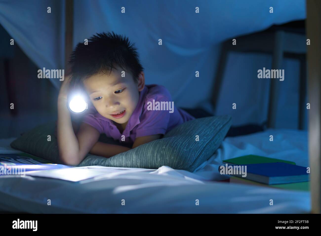 Enfant d'âge préscolaire asiatique faire un camp pour jouer imaginatif et lire livre par lampe de poche dans le salon à la maison. Banque D'Images
