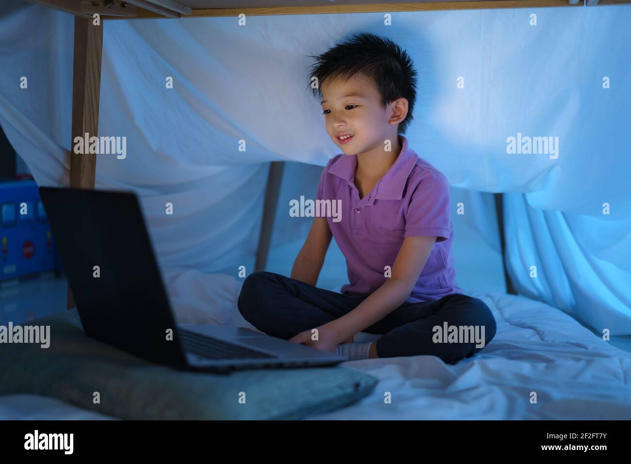 Enfant asiatique de faire un camp pour jouer imaginatif en regardant un film sur ordinateur portable dans l'obscurité du camp dans le salon à la maison. Banque D'Images