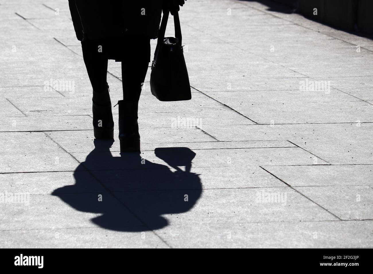 Silhouette noire et ombre d'une femme solitaire avec sac à main marchant dans une rue. Concept de la mode féminine et des chaussures Banque D'Images