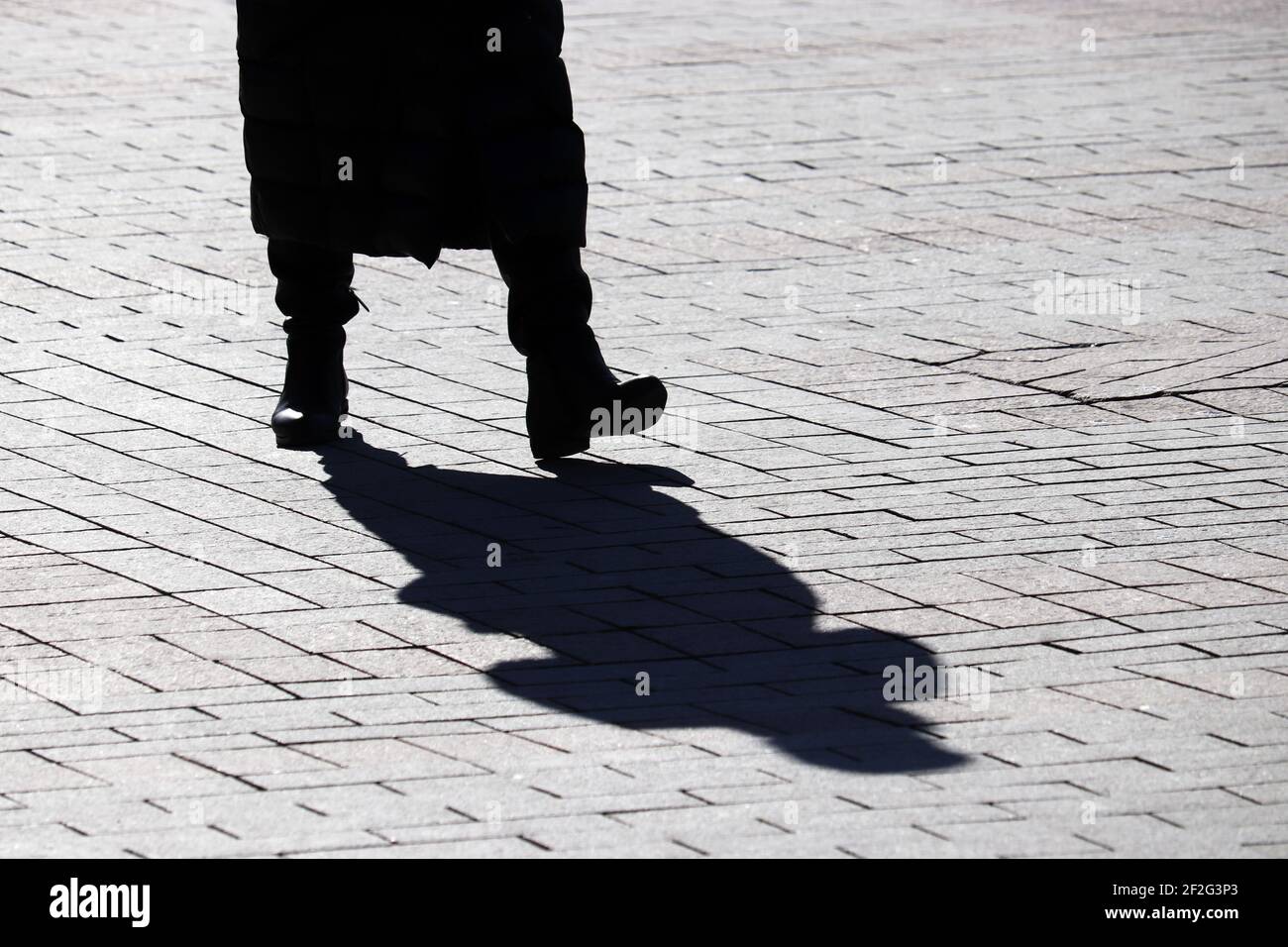 Silhouette noire et ombre d'une femme dans une longue veste en duvet marchant dans une rue. Concept de temps froid, mode féminine Banque D'Images