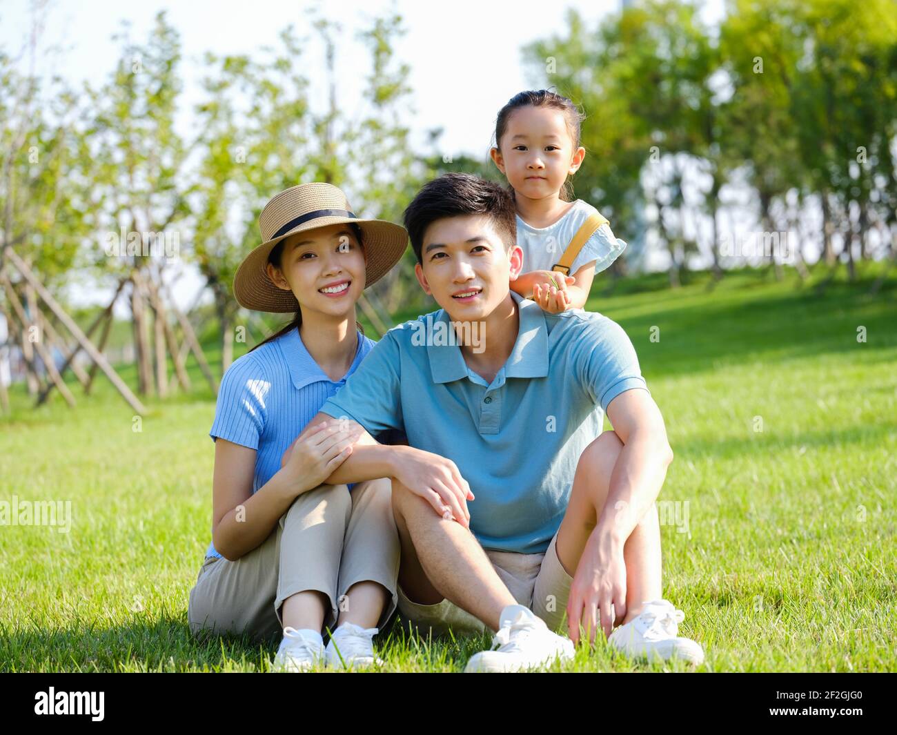 Bonne famille de trois personnes assises sur l'herbe souriante Banque D'Images