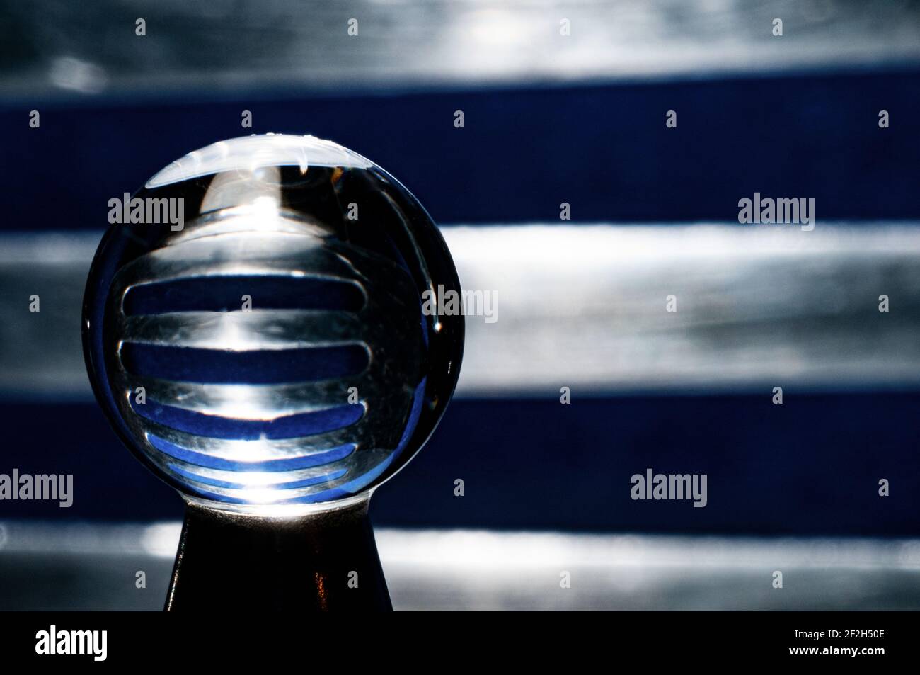 Sphère en verre sur fond bleu avec réflexion de grille métallique Banque D'Images