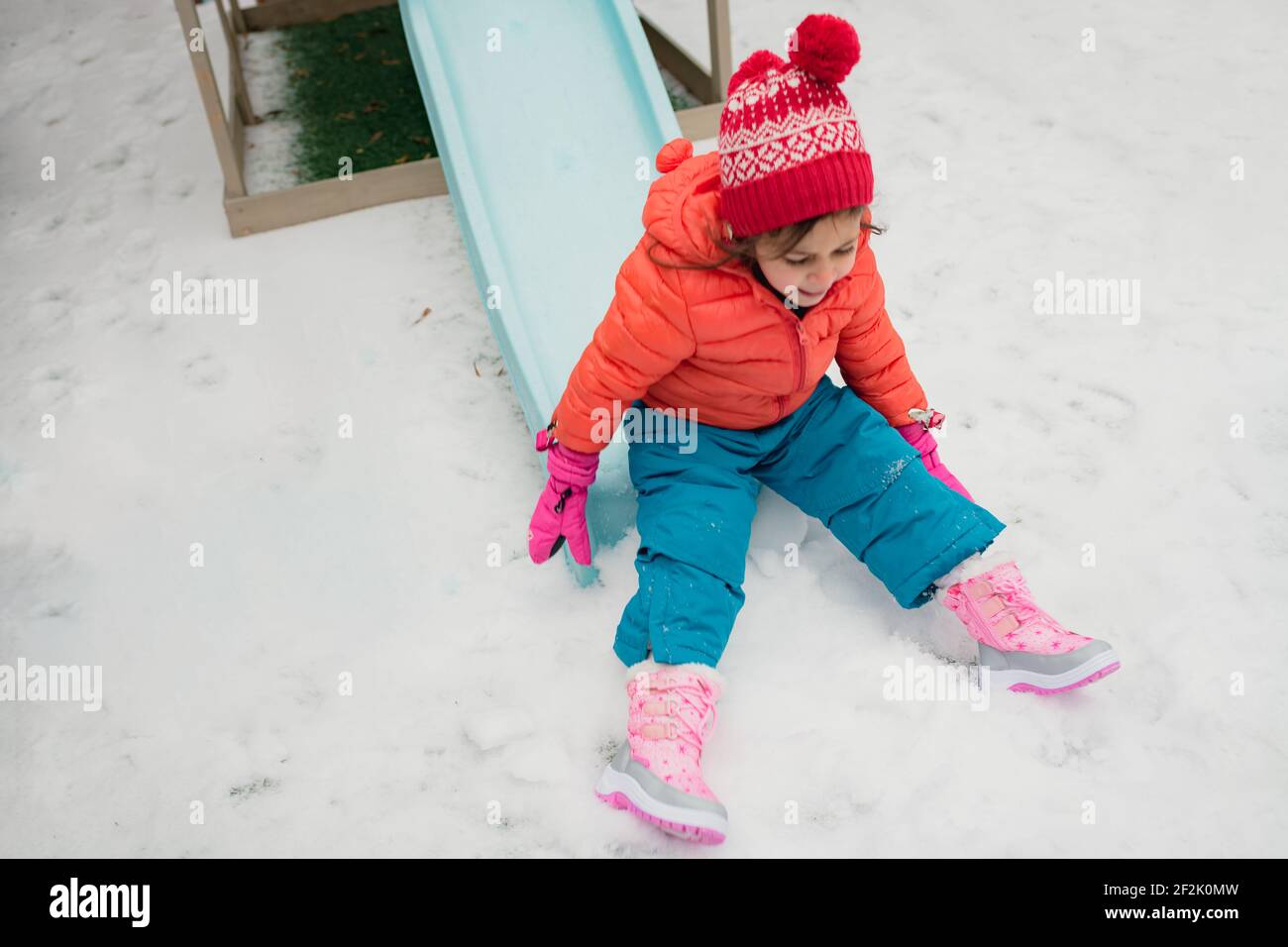 Une jeune fille d'âge préscolaire jouant sur la diapositive le jour de neige Banque D'Images