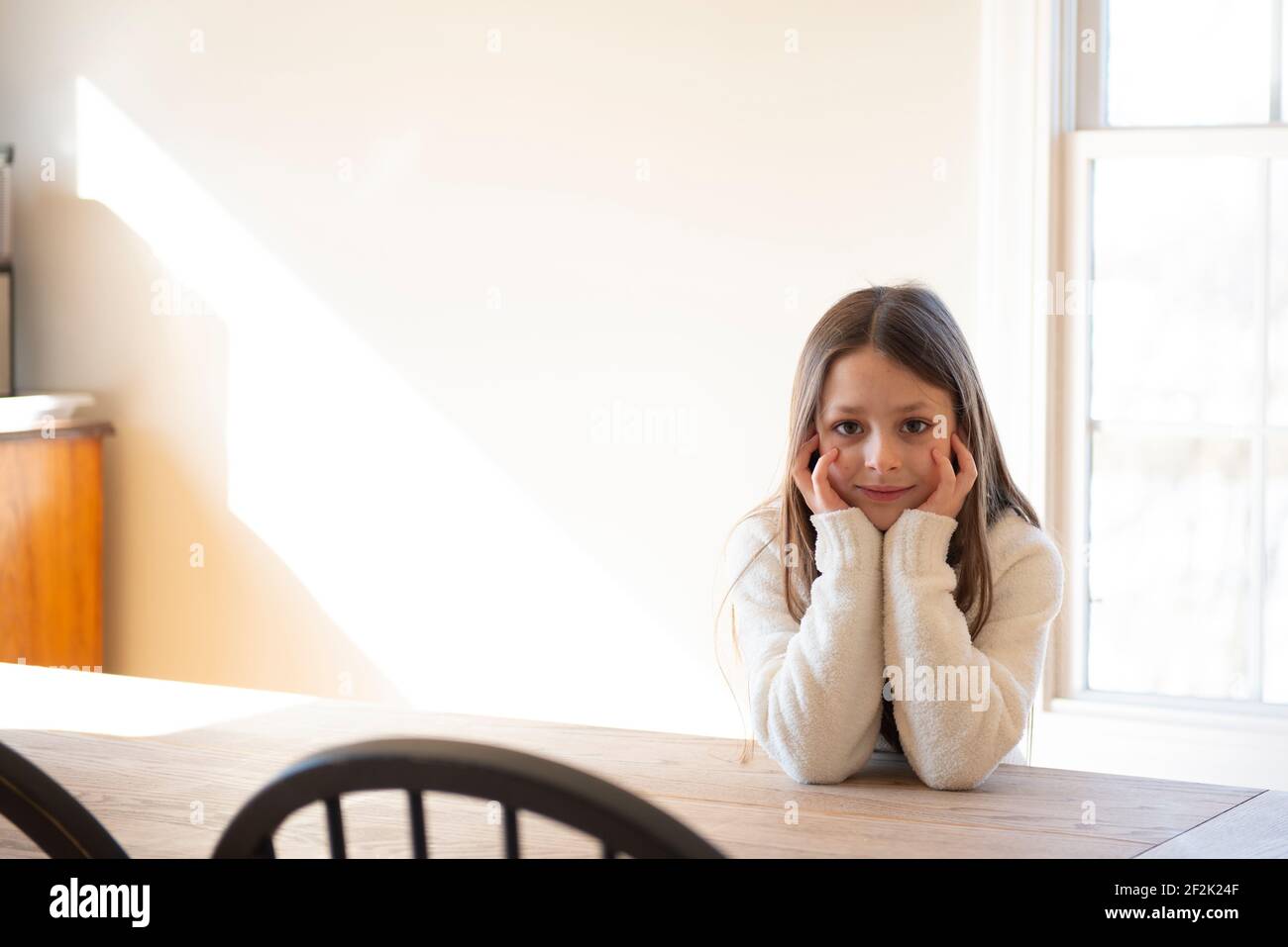 Belle fille assise à une table de ferme au soleil. Banque D'Images