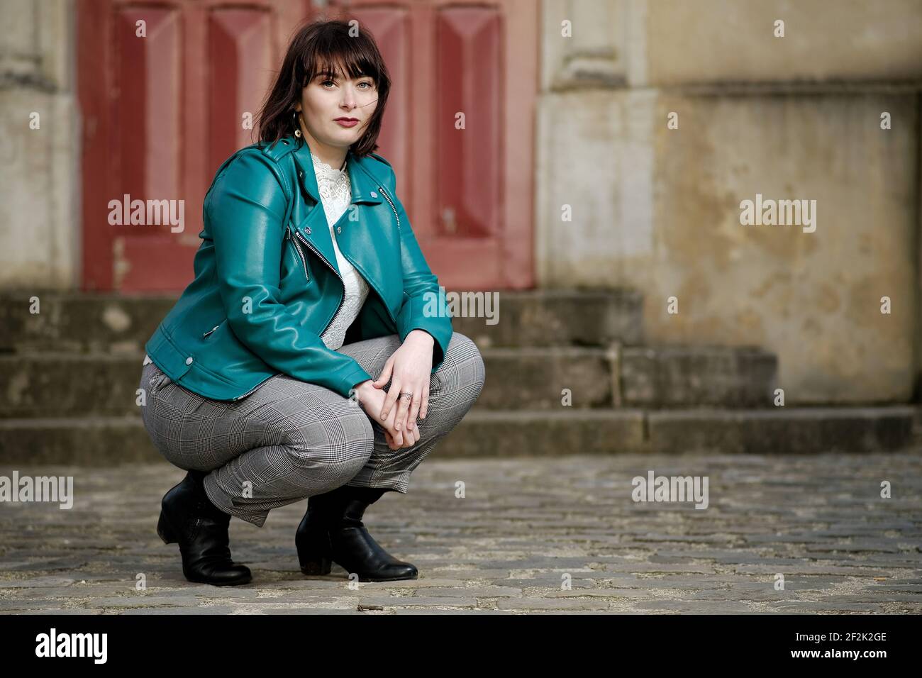 Belle jeune parisienne avec des yeux verts et un vert Veste devant une porte rouge à Paris Banque D'Images