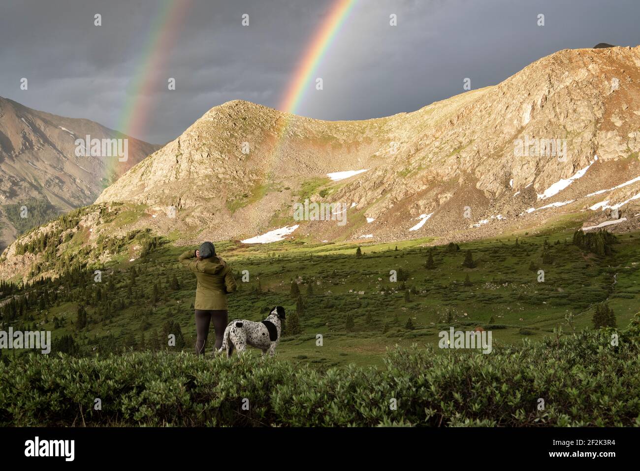 Vue arrière d'une femme qui regarde le double arc-en-ciel pendant la randonnée avec chien pendant les vacances Banque D'Images