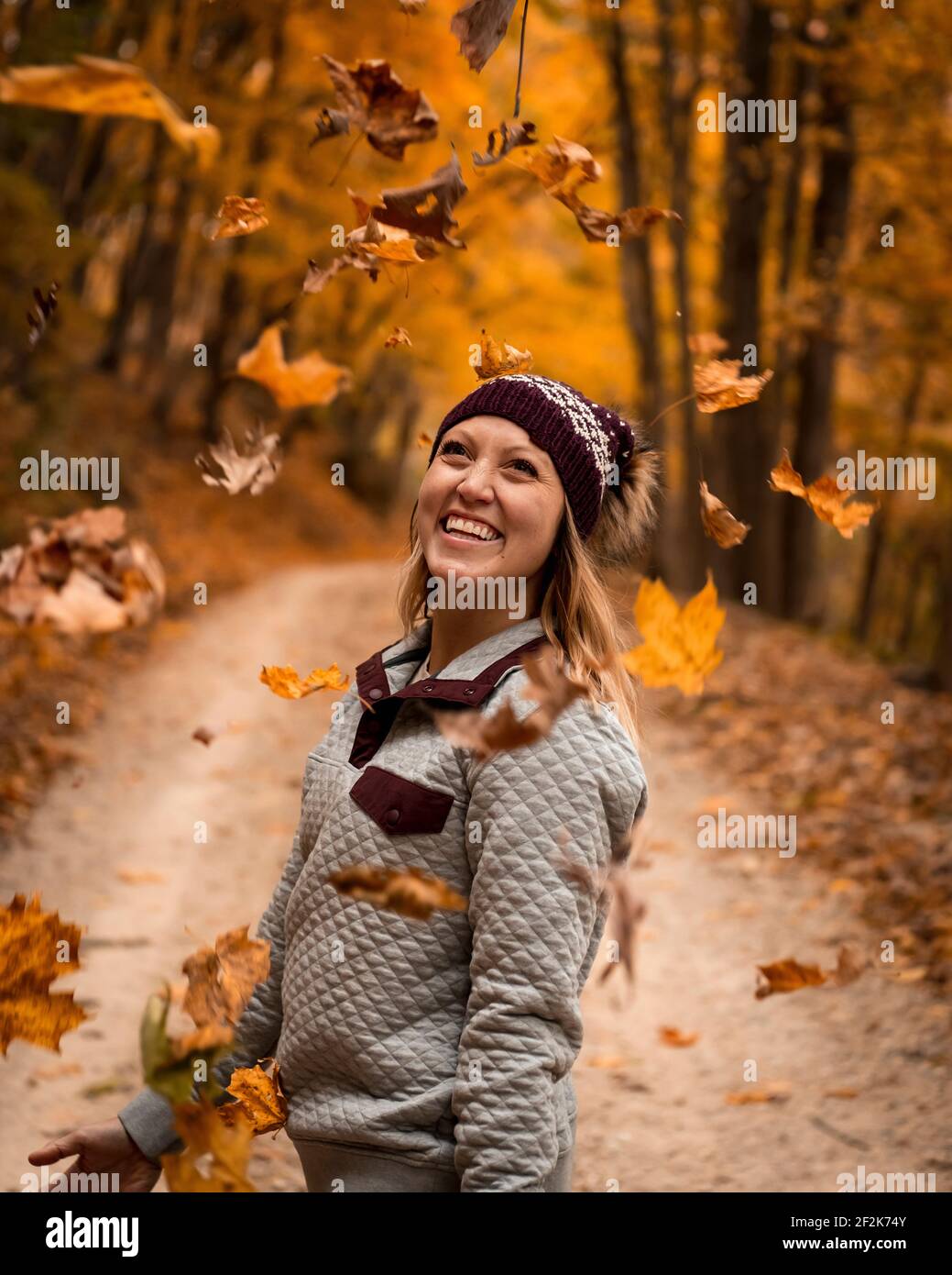Jeune femme joyeuse jetant des feuilles d'automne tout en appréciant des vacances dans forêt Banque D'Images