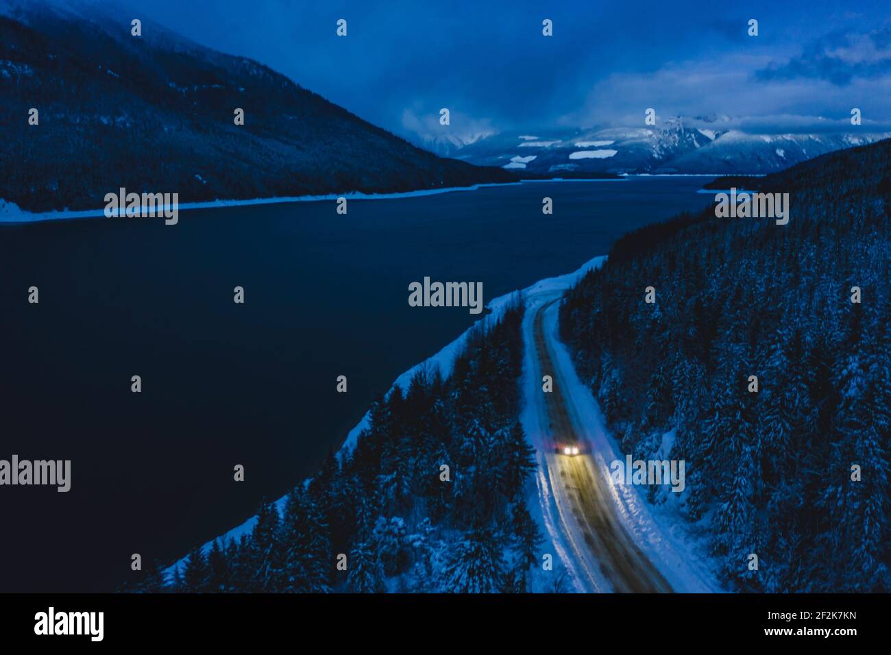 Voiture se déplaçant sur la route par la rivière pendant l'hiver au crépuscule Banque D'Images