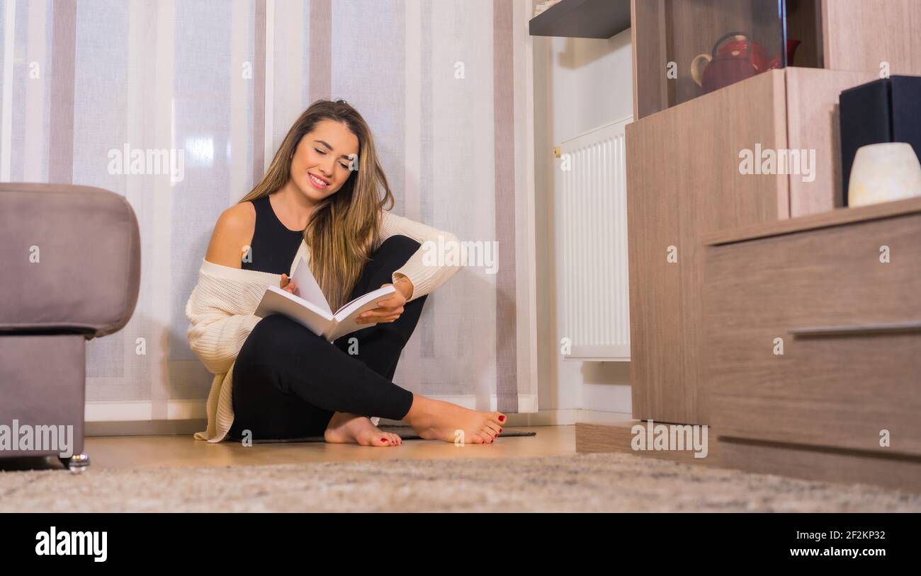 Une femme espagnole assise sur le sol et lisant un réservez dans son salon Banque D'Images