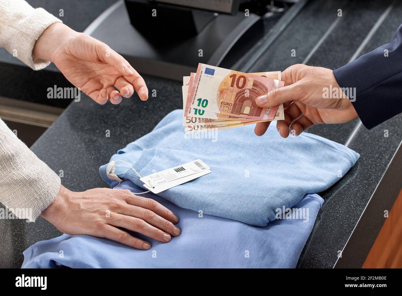Un client mâle remet des billets € au guichet d'un magasin de mode, une femme vendeuse dans un magasin de textile, seulement les mains visibles Banque D'Images
