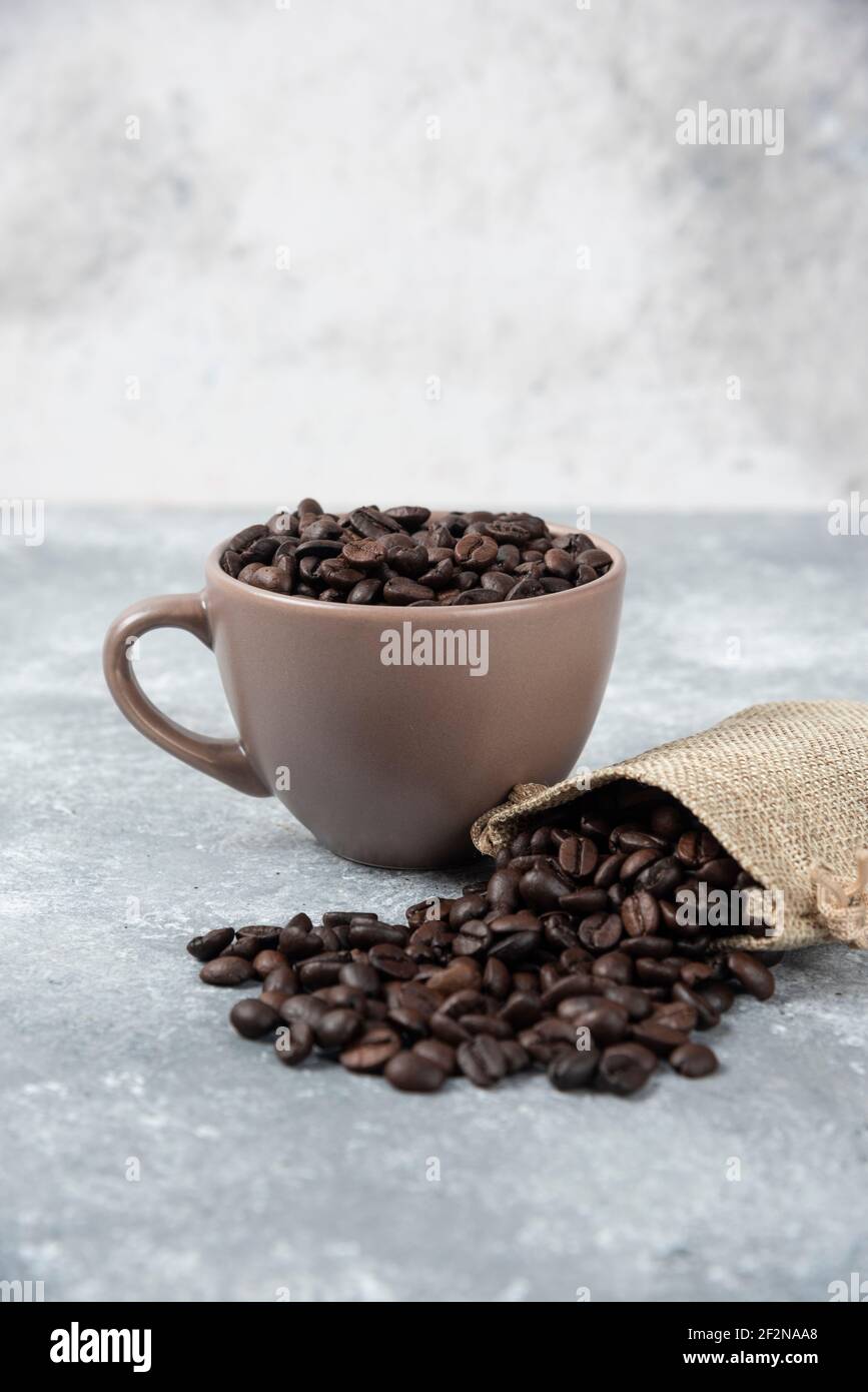 Grains de café torréfiés dans un sac de toile de jute et dans une tasse sur fond de marbre Banque D'Images