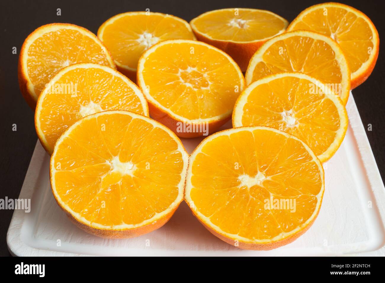 Belle composition d'oranges fraîches coupées en deux sur une planche à découper blanche sur la table de cuisine sombre. Préparation de jus sains. Banque D'Images