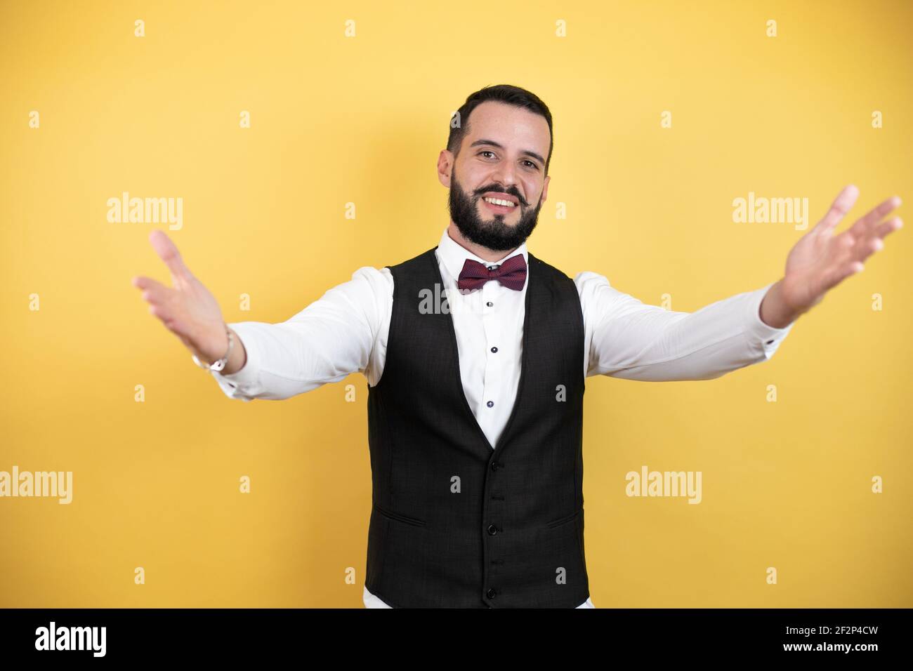 Jeune homme avec une barbe portant un noeud papillon et un gilet à  l'appareil photo en souriant avec les bras ouverts pour le câlin Photo  Stock - Alamy