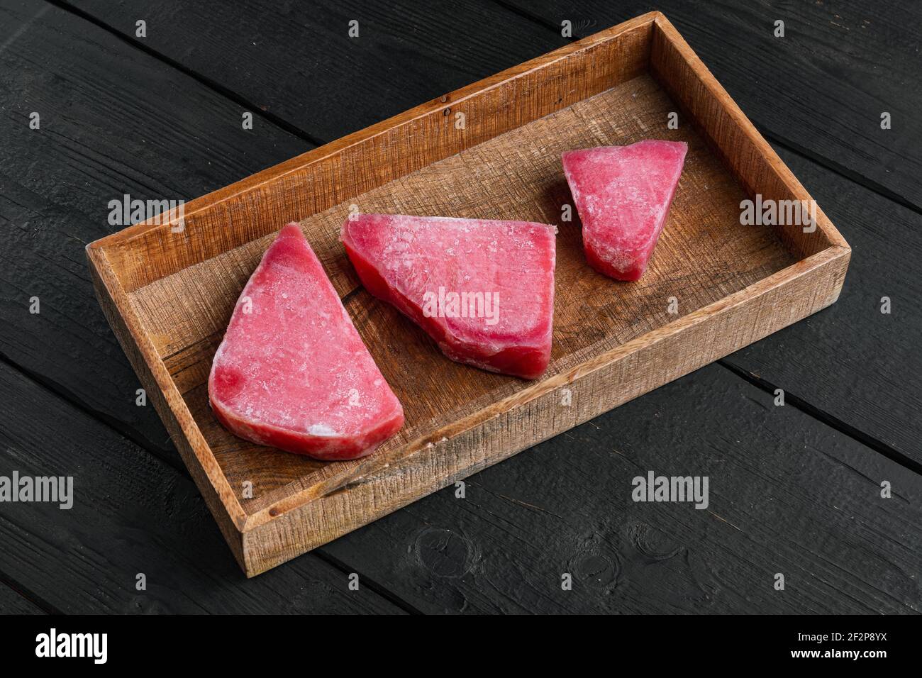 Ensemble de steaks de thon surgelé, dans une boîte en bois, sur fond en bois noir Banque D'Images