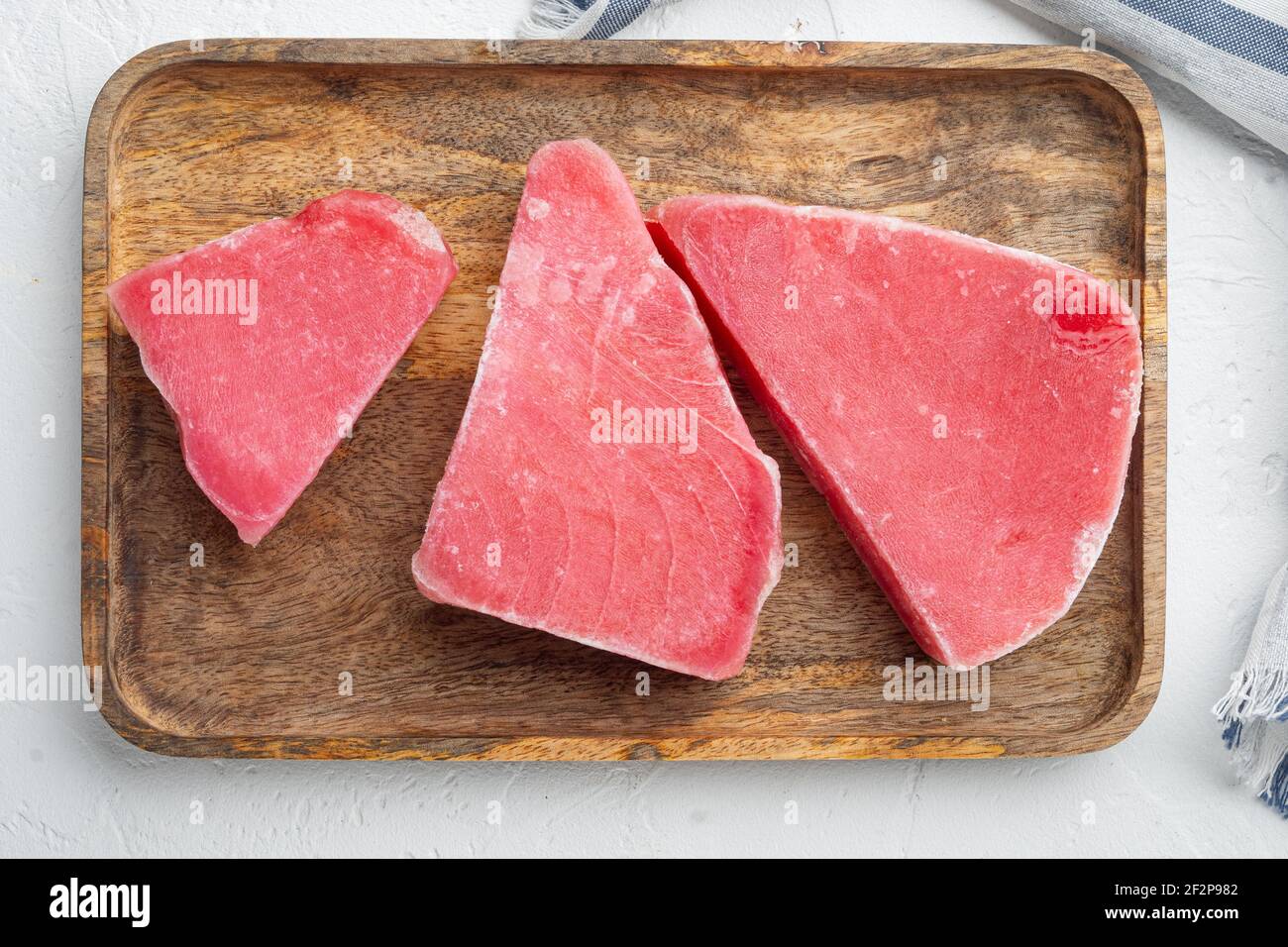 Ensemble de steaks de thon surgelé, sur plateau en bois, sur fond de pierre blanche, plan de dessus Banque D'Images