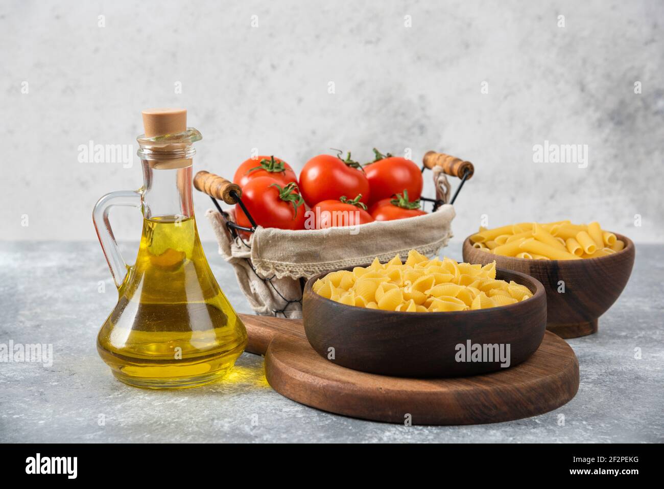 Bols en bois de diverses pâtes crues et tomates fraîches arrière-plan en marbre Banque D'Images