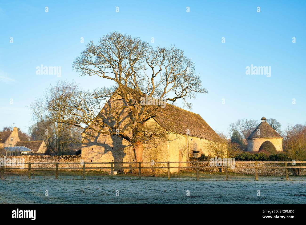 Lever de soleil sur un arbre d'hiver devant une grange dans le gel. Minster Lovell, Oxfordshire, Angleterre Banque D'Images