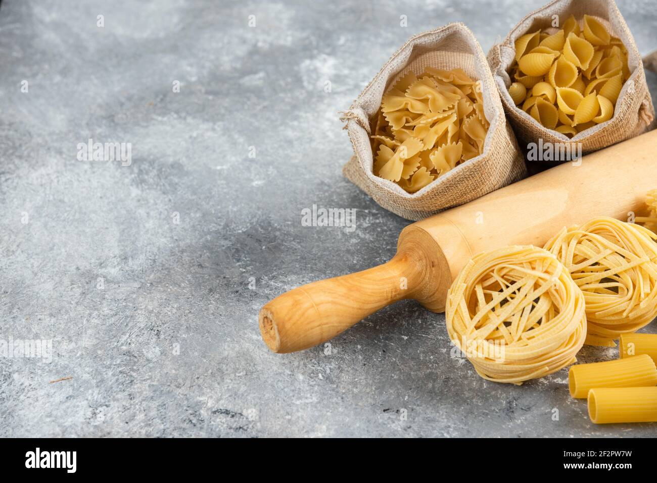 Variétés de pâtes dans un panier rustique avec un rolling rose en bois sur fond de marbre Banque D'Images