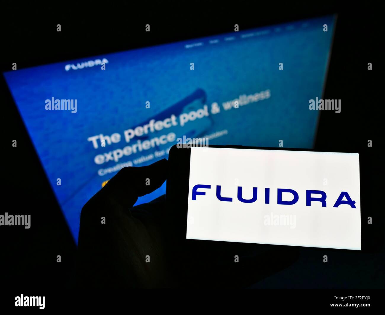 Personne tenant un téléphone mobile avec le logo d'affaires de la compagnie espagnole de piscine Fluidra S.A. sur l'écran en face de la page web. Mise au point sur l'affichage du téléphone. Banque D'Images