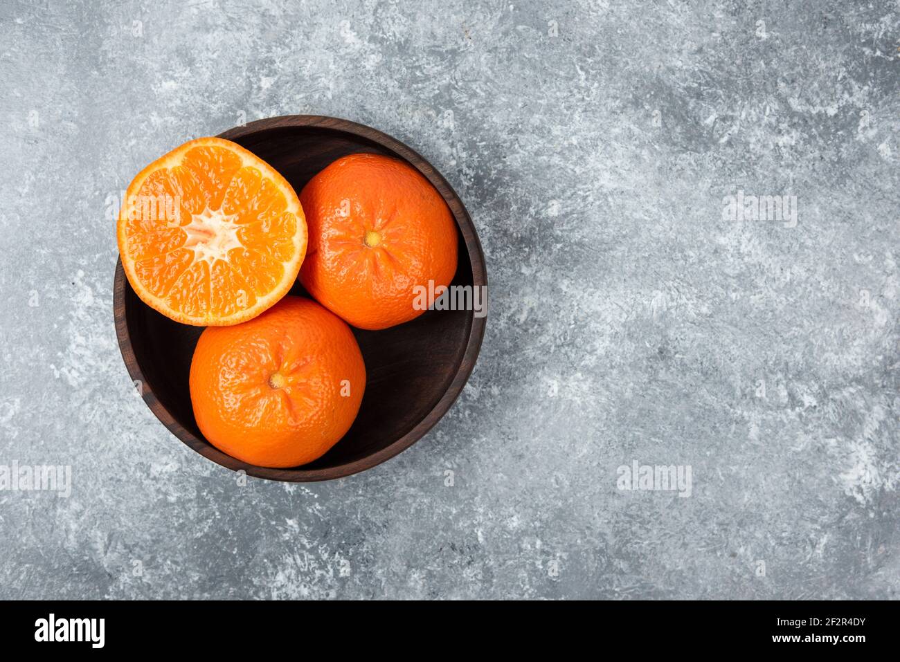 Un bol en bois plein de fruits d'orange juteux sur pierre arrière-plan Banque D'Images
