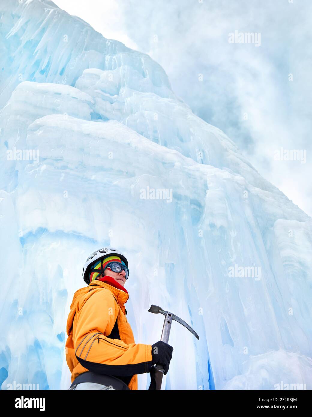 Femme grimpante en veste orange avec glace hache près de gelé cascade dans les montagnes Banque D'Images