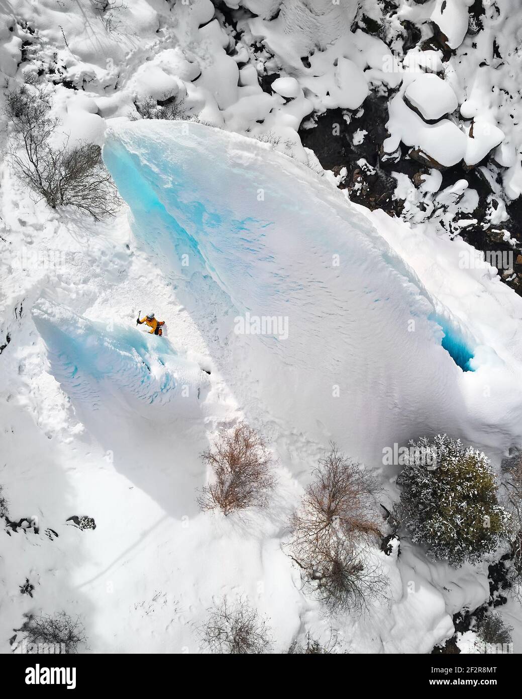 Photo aérienne d'une femme grimpant une chute d'eau gelée avec une hache de glace en veste orange dans les montagnes Banque D'Images