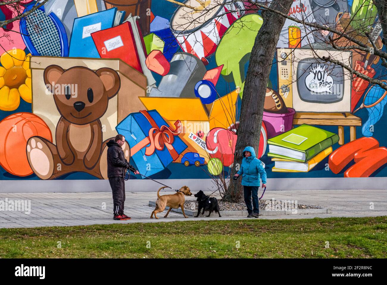 Deux personnes se rencontrent avec leurs chiens devant la façade colorée d'un bâtiment de grande hauteur au centre de la ville. Banque D'Images