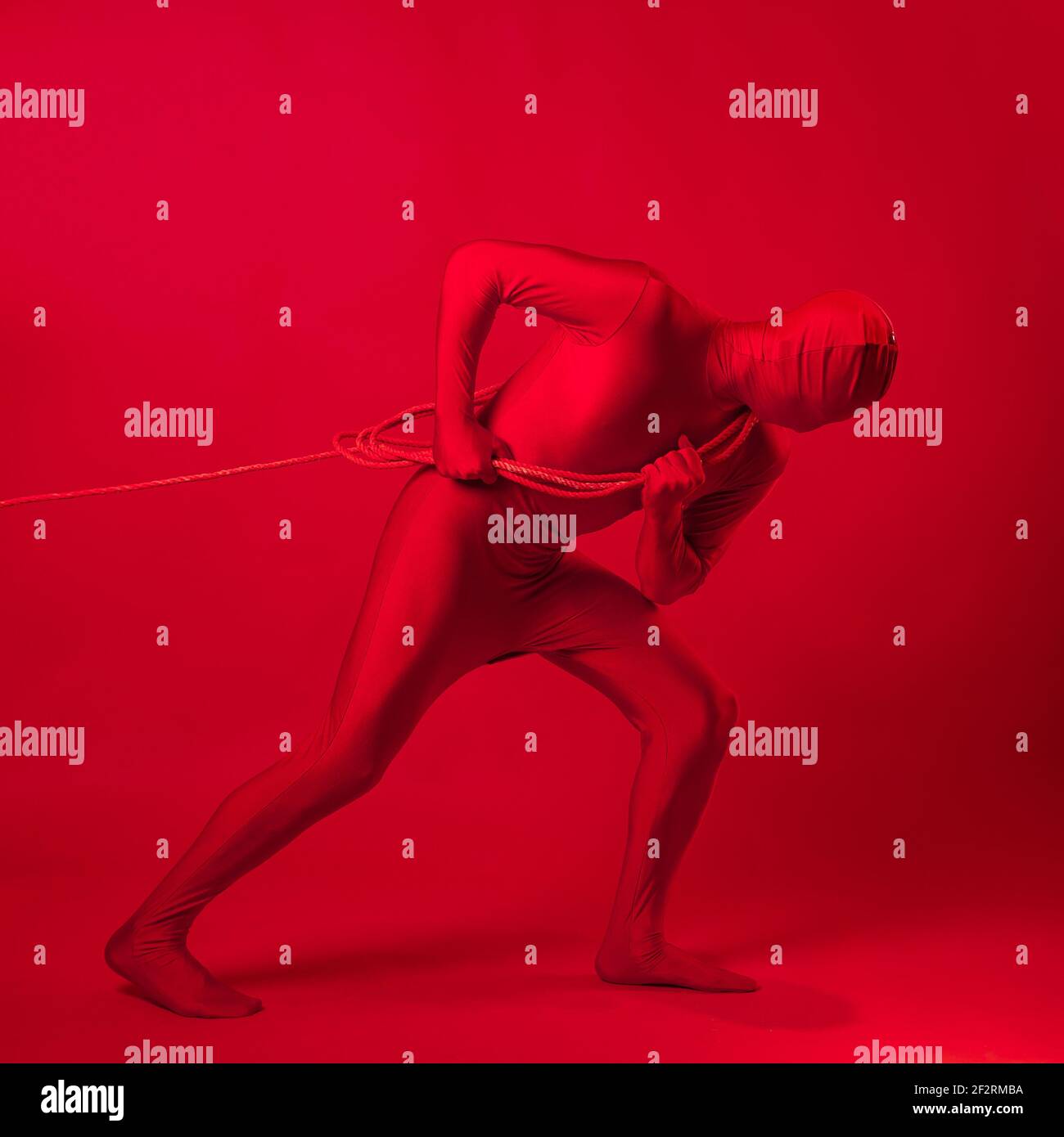 Un homme rouge anxieux dans un léopard rouge, traînant un lourd fardeau, tirant une lourde charge avec une corde. Le concept de stress et de surmenage au travail. Banque D'Images Un homme rouge anxieux dans un léopard rouge, traînant un lourd fardeau, tirant une lourde charge avec une corde. Le concept de stress et de surmenage au travail. Banque D'Images