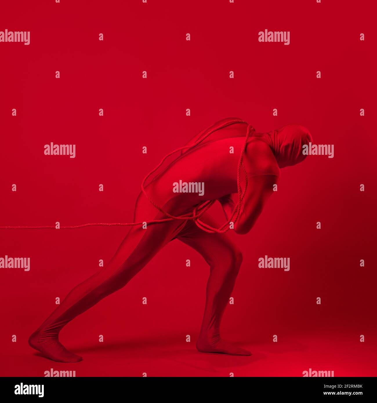 Un homme rouge anxieux dans un léopard rouge, traînant un lourd fardeau, tirant une lourde charge avec une corde. Le concept de stress et de surmenage au travail. Banque D'Images Un homme rouge anxieux dans un léopard rouge, traînant un lourd fardeau, tirant une lourde charge avec une corde. Le concept de stress et de surmenage au travail. Banque D'Images