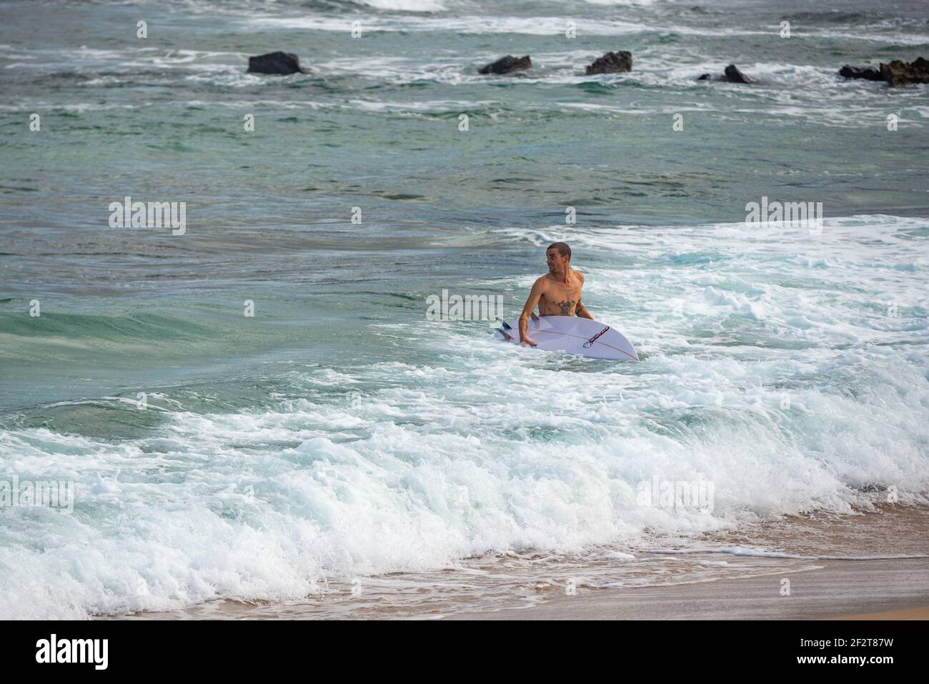 Homme sortant de l'océan près de la plage de Famara Lanzarote avec planche de surf sous son bras Banque D'Images