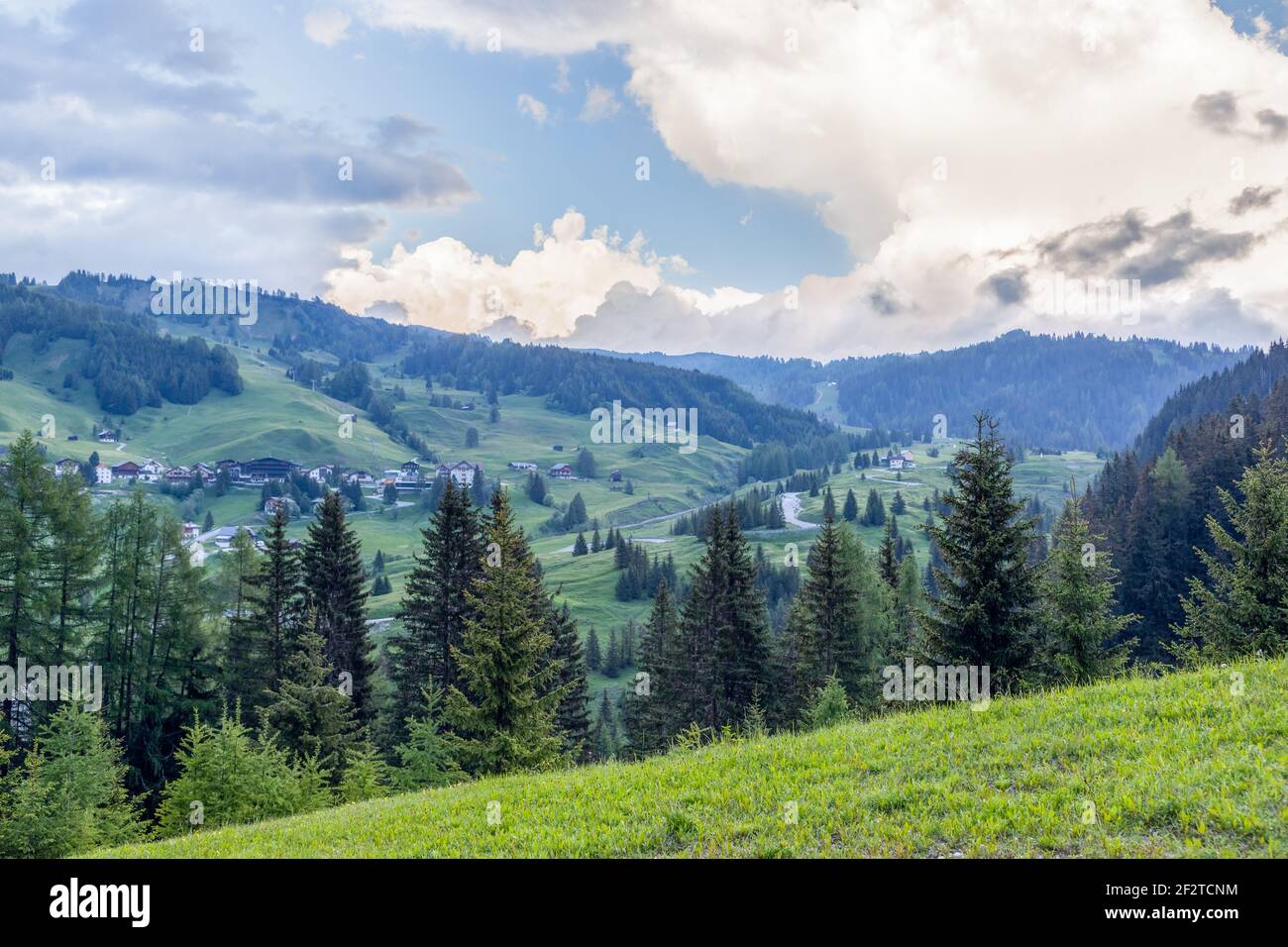 Des prairies alpines verdoyantes et des chalets éparpillés s'étendent au-delà des conifères sous les nuages du soir près de Corvara in Badia, Dolomites, Trentin-Haut-Adige, Italie. Banque D'Images