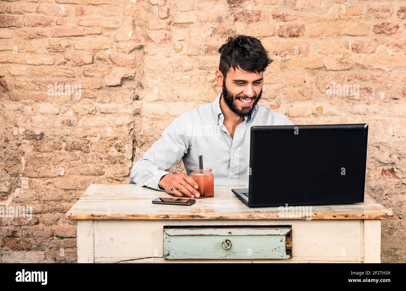 Jeune homme taille basse avec moustache assis au bureau vintage avec ordinateur portable dans grunge bureau alternatif - concept de début travailler en entreprise Banque D'Images