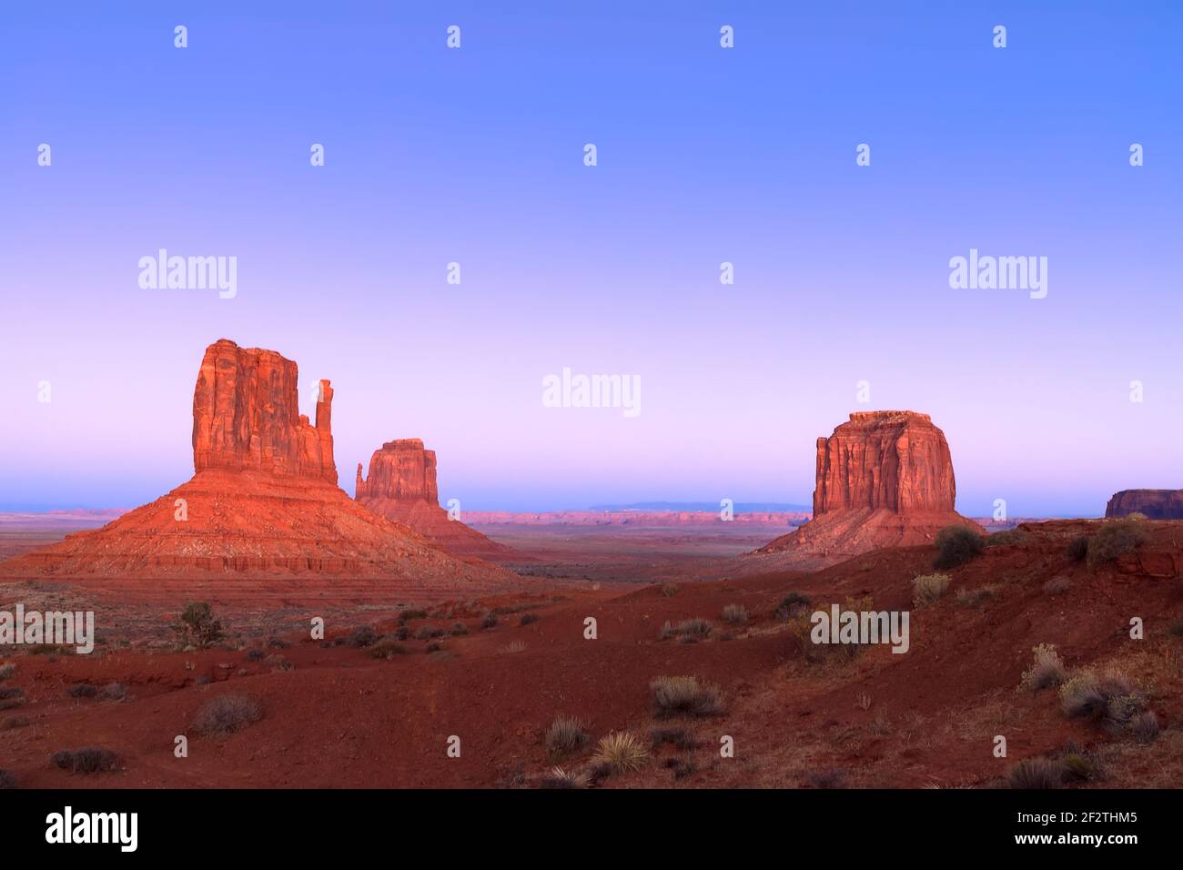 La lumière du soir réchauffe les buttes Mitten et Merrick sous un ciel rose et bleu dans le Monument Valley Navajo Tribal Park, Arizona, États-Unis. Banque D'Images