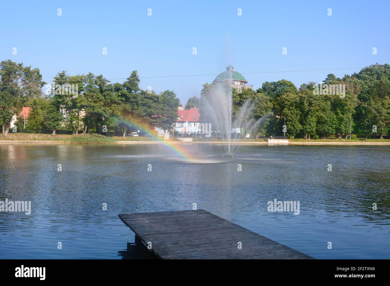 Parc de la ville avec jetée sur le lac. Fontaine avec eau éclabousse et arc-en-ciel. Mise au point sélective, flou. Banque D'Images