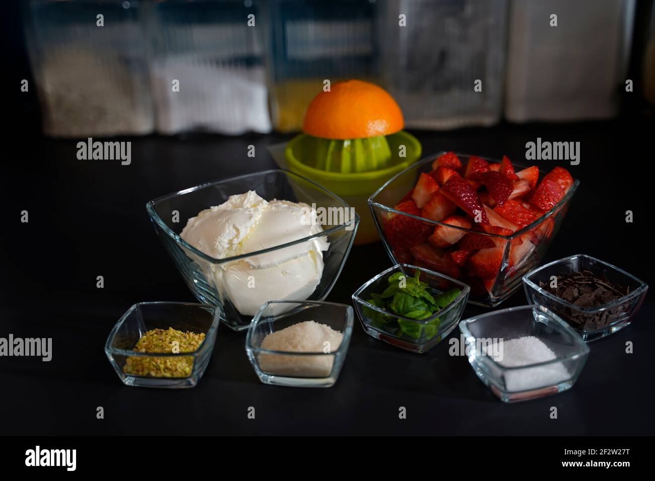 Ingrédients pour un dessert avec double fromage à la crème, fraises, pistaches hachées, sucre, orange, copeaux de menthe et de chocolat disposés en bo Banque D'Images