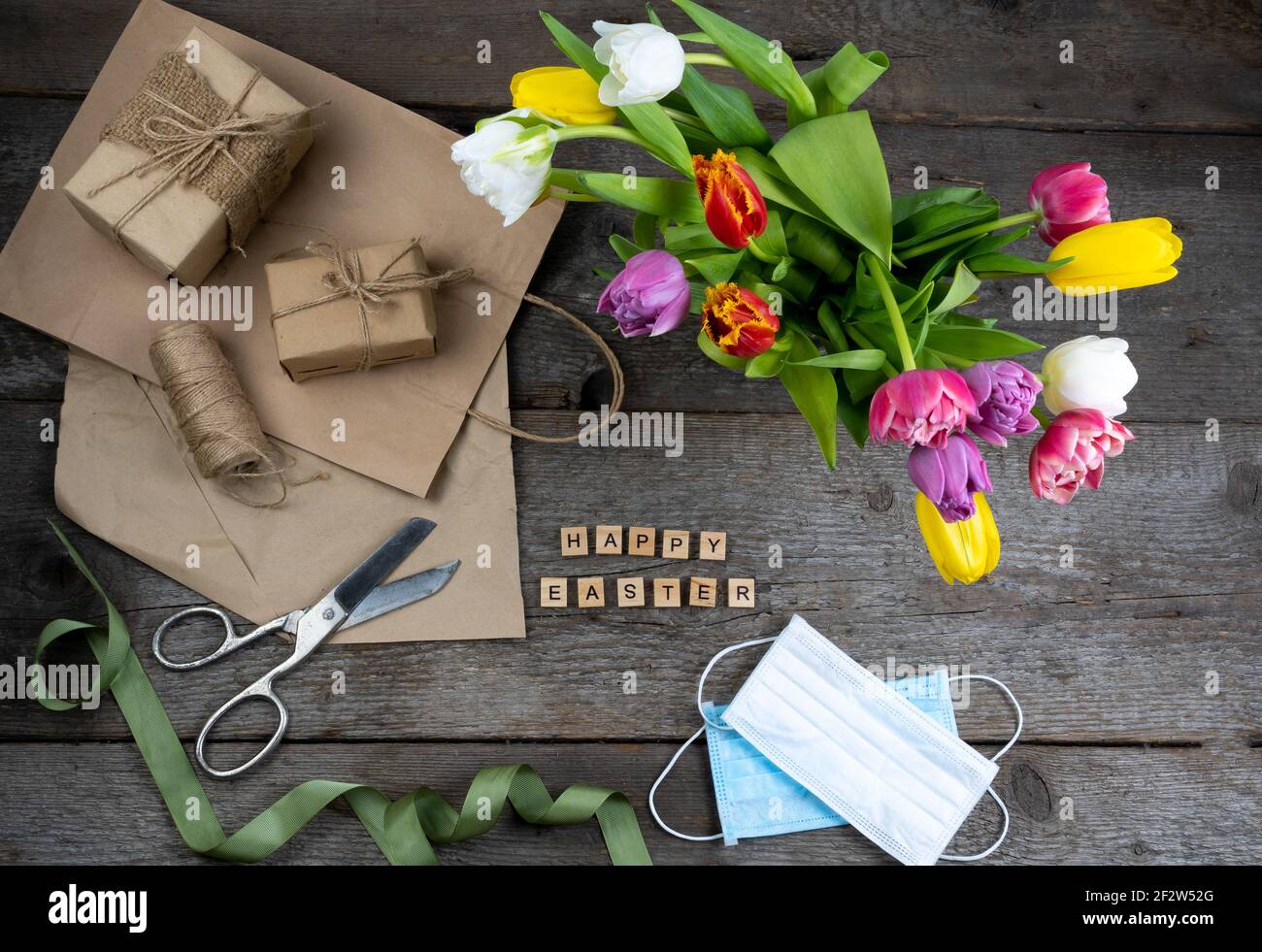 Expression Joyeuses Pâques. Emballage cadeau pour les vacances. Bouquet de tulipes sur fond de bois. Masques médicaux. Papier cadeau et emballage. Vue de dessus m Banque D'Images