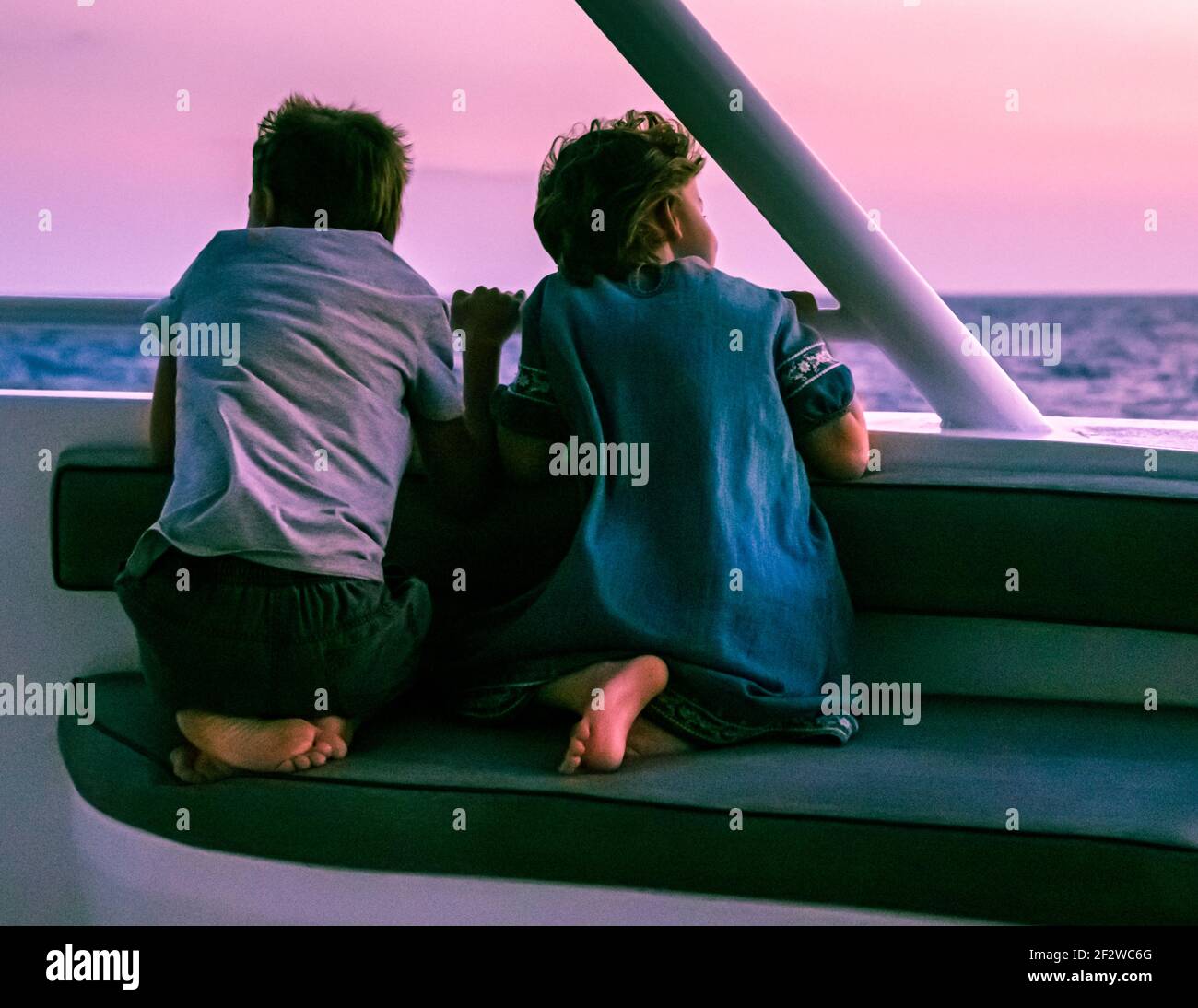 Deux jeunes enfants sont assis sur un banc sur le pont du True North sous la lumière violette du soir, contemplant l'horizon, East Nusa Tenggara, Indonésie. Banque D'Images
