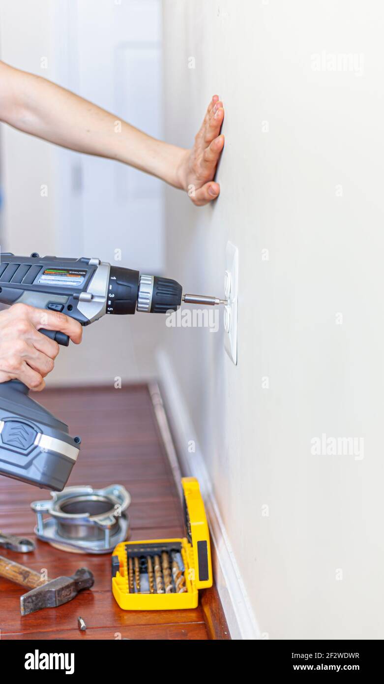Une femme utilise une perceuse électrique sans fil avec un tournevis embout fixé pour retirer la vis maintenant le couvercle d'une prise électrique sur le Banque D'Images
