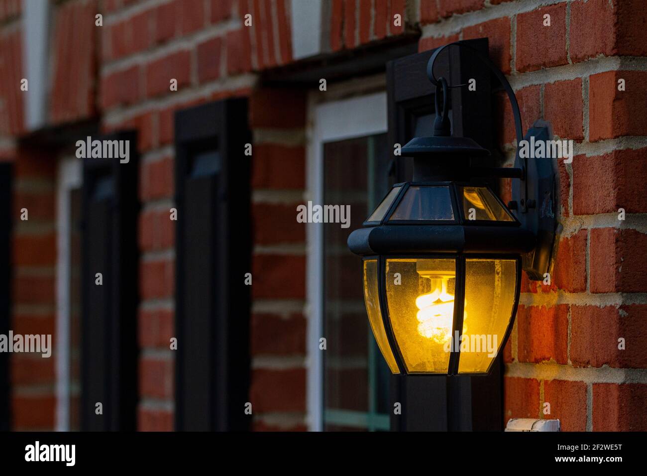 Ampoule fluorescente compacte en spirale luminescent. L'ampoule se trouve à l'intérieur d'une lanterne murale en métal fixée au mur de briques de l'extérieur d'une maison Banque D'Images