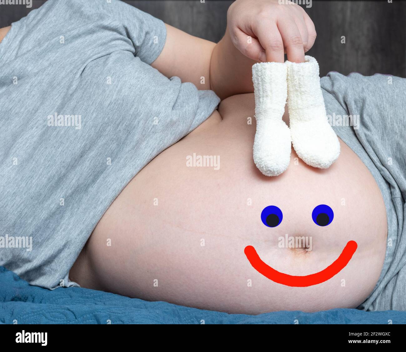 Juste pour le plaisir. Une femme enceinte tenant bébé tricoté petites  chaussettes dans ses mains et un sourire heureux dessiné sur son ventre.  Concept de grossesse joyeuse Photo Stock - Alamy