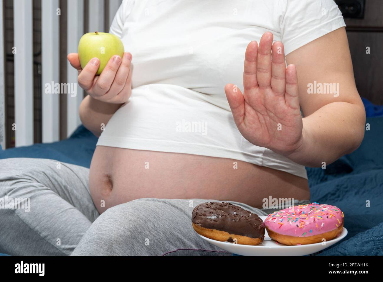 Gros plan d'une femme enceinte tenant une pomme verte dans ses mains, refusant les beignets. Concept d'alimentation saine pendant la grossesse. Concept de contrôle du poids. Banque D'Images