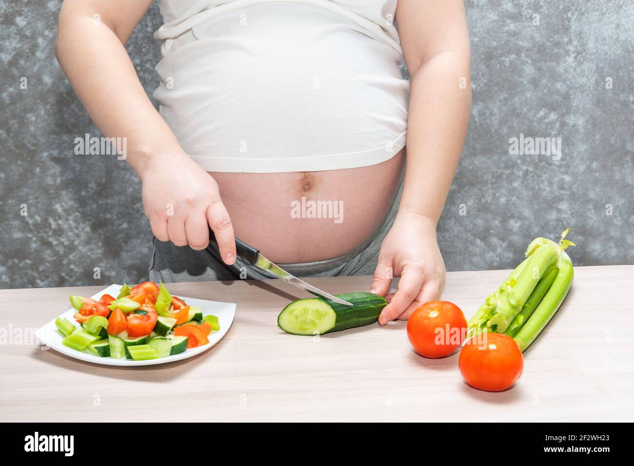 Femme enceinte coupant le concombre pour une salade verte fraîche, femme  prépare un délicieux dîner biologique à la maison, une alimentation saine  pour la future mère. Concept de h Photo Stock -