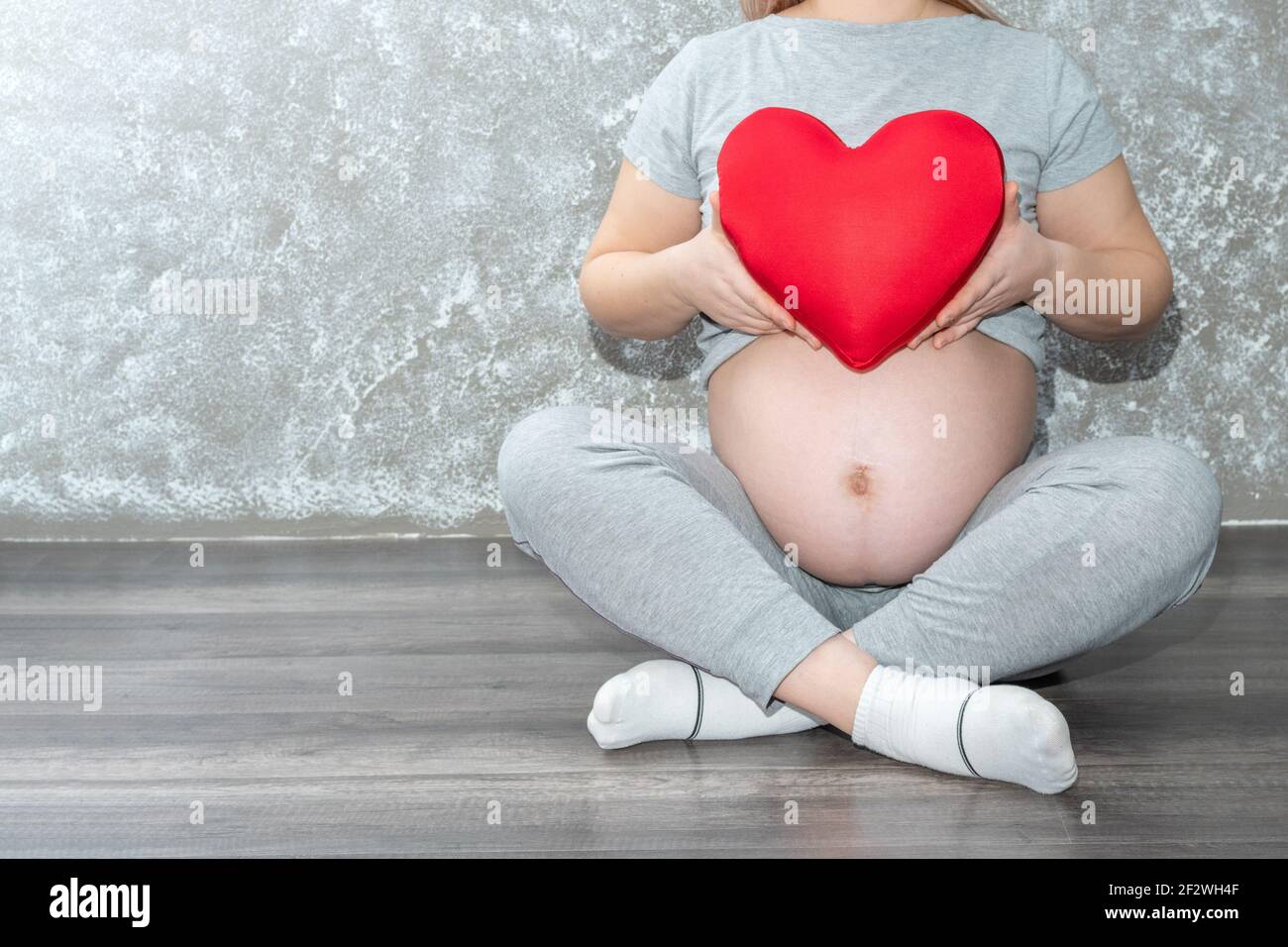 Grossesse, maternité, personnes, amour et attente concept - gros plan d'une femme enceinte tenant un coussin en forme de cœur rouge à la maison. Une femme enceinte Banque D'Images