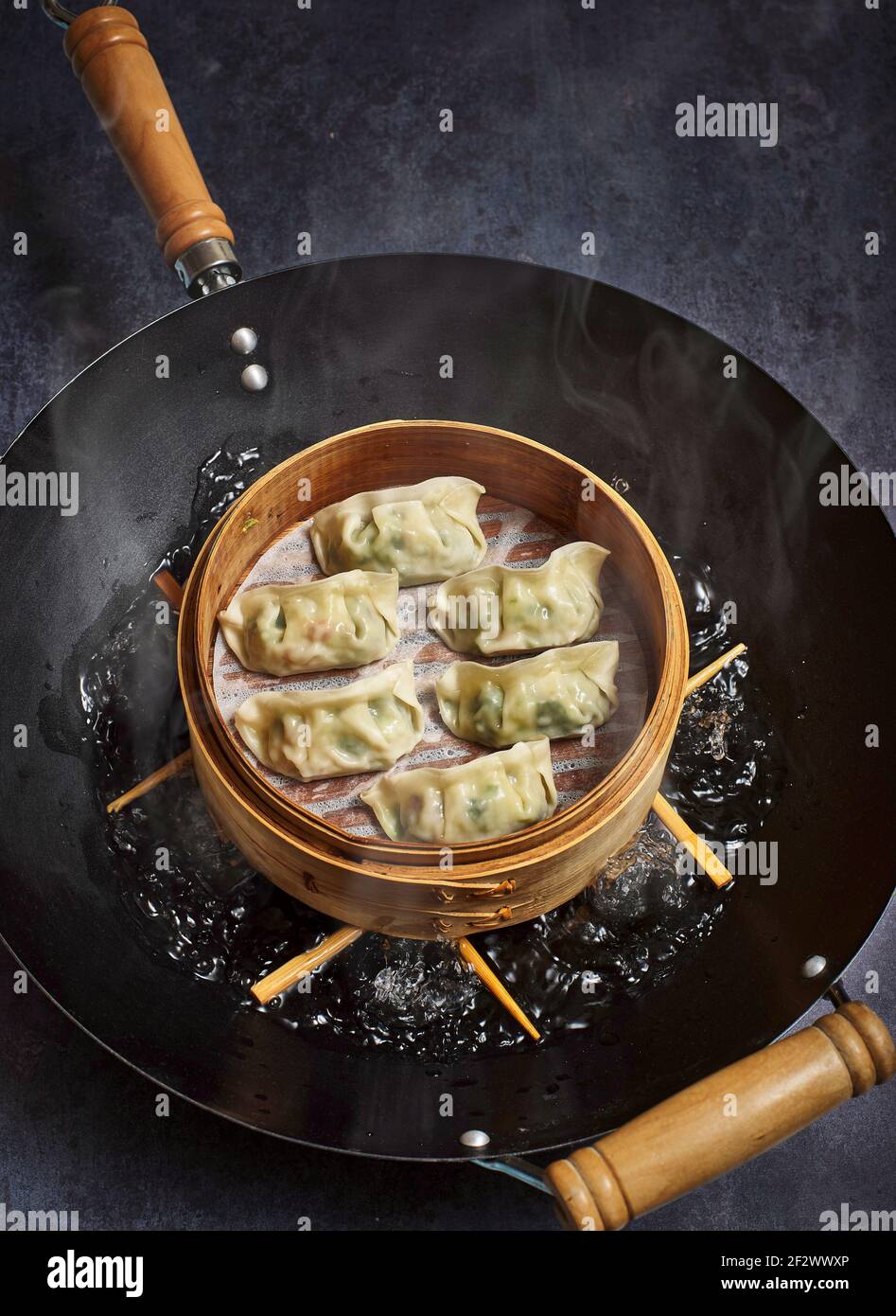 Boulettes de gyoza cuisant dans un cuiseur vapeur en bambou sur un wok. Banque D'Images