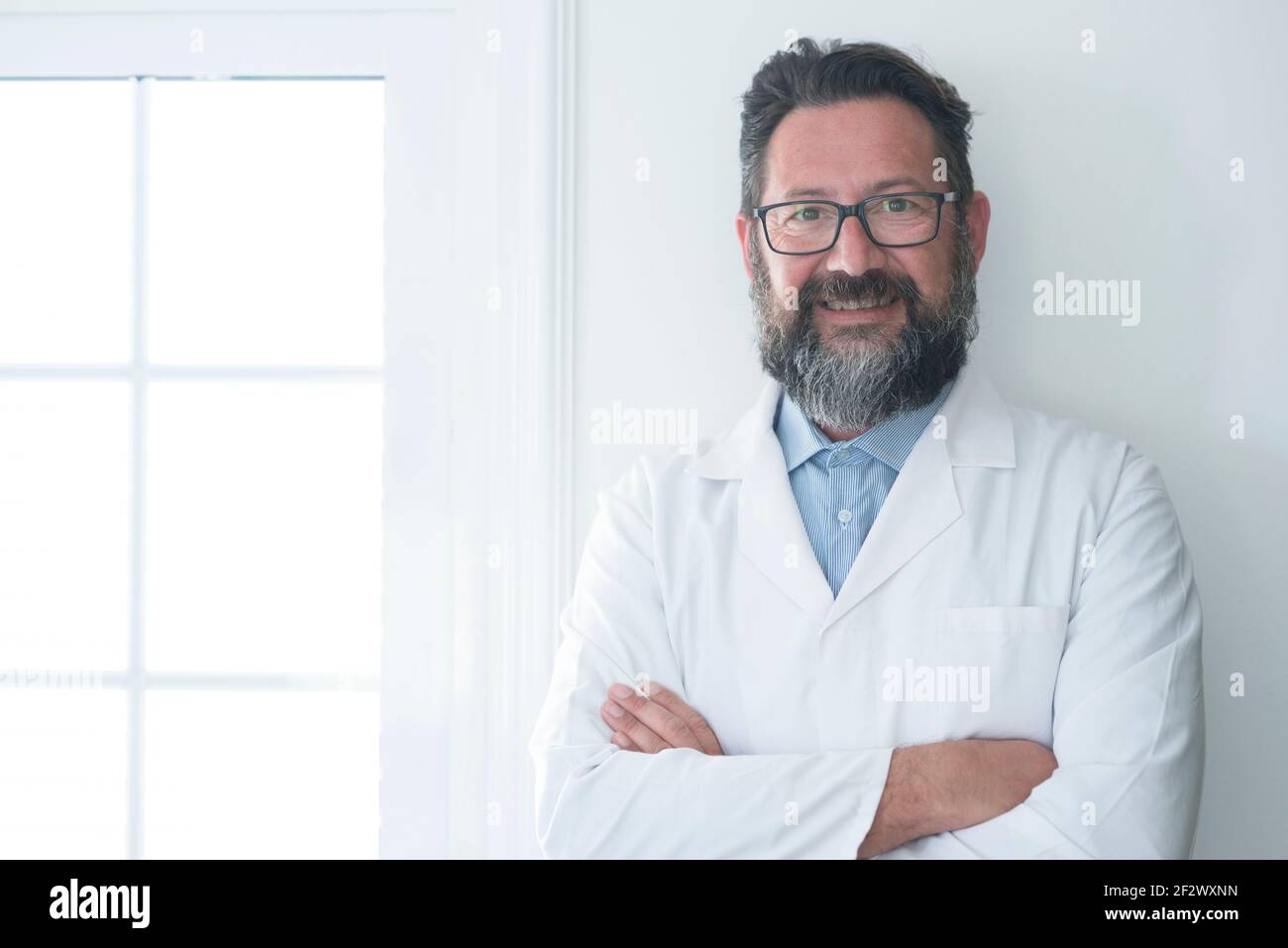 Gai mature médecin posant et souriant à la caméra, les soins de santé et la médecine - adulte homme gai avec l'hôpital regarder debout et regardant - la santé vis Banque D'Images